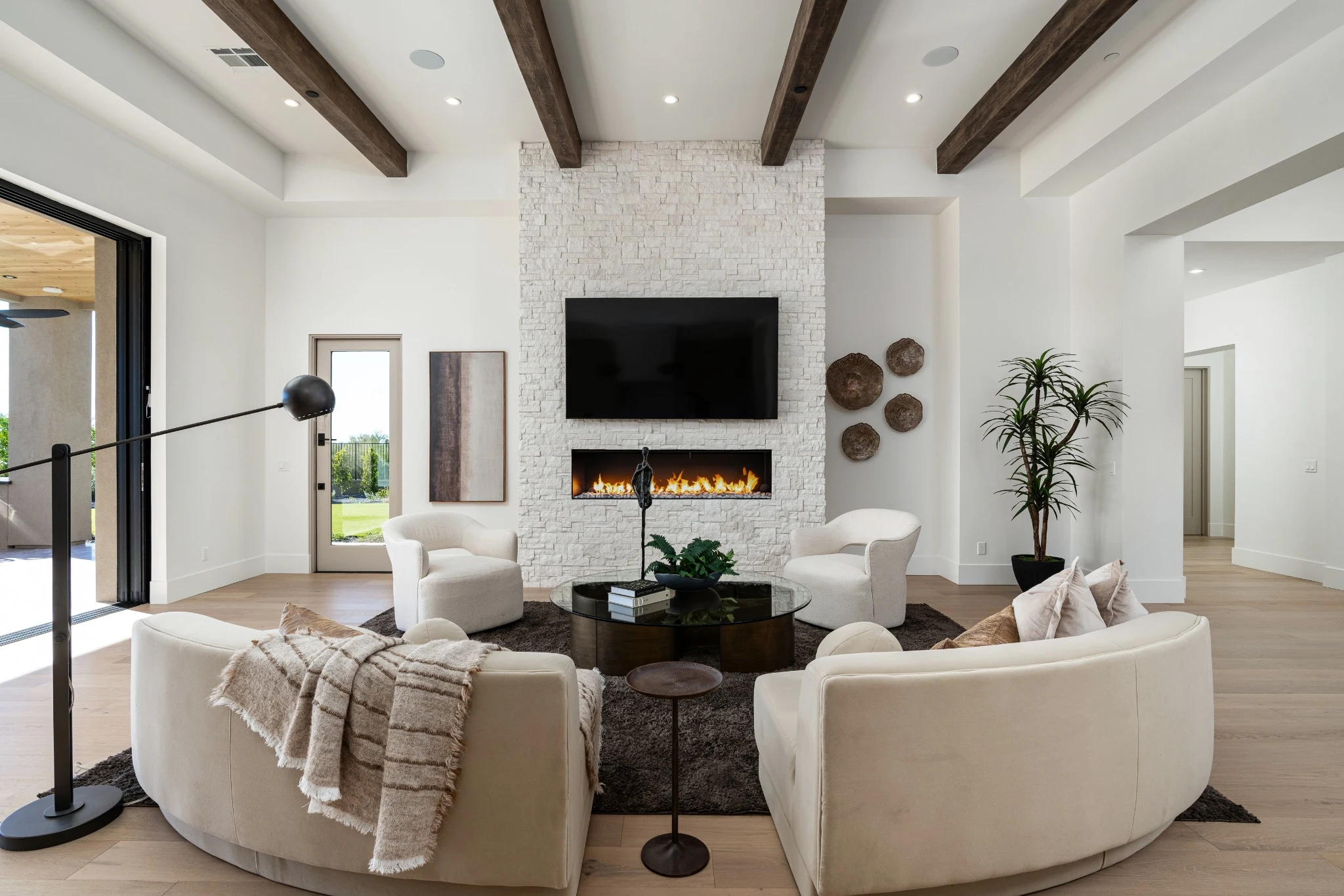 Living room with curved linen sofas, timber beams, and a textured stone fireplace