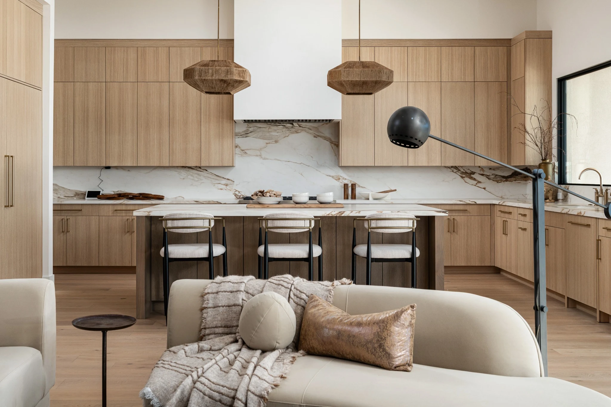Warm oak cabinetry and woven pendants frame a light-filled kitchen and soft, sculptural seating