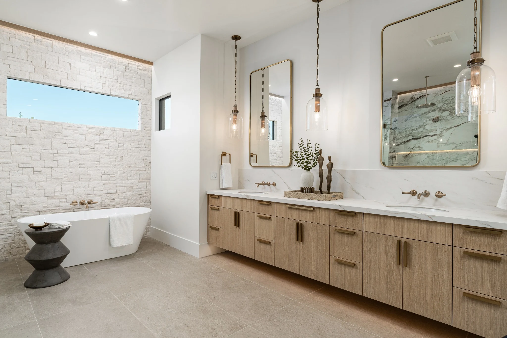 Primary bathroom with pale oak cabinetry, wall sconces, and a freestanding bath